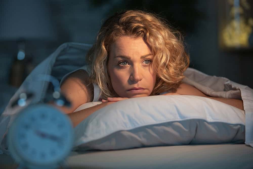 Insomnia Treatment — woman lying awake in bed at night unable to sleep.