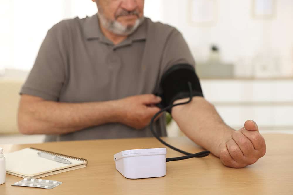 Obesity and High Blood Pressure — man checking his blood pressure at home with a monitor cuff.