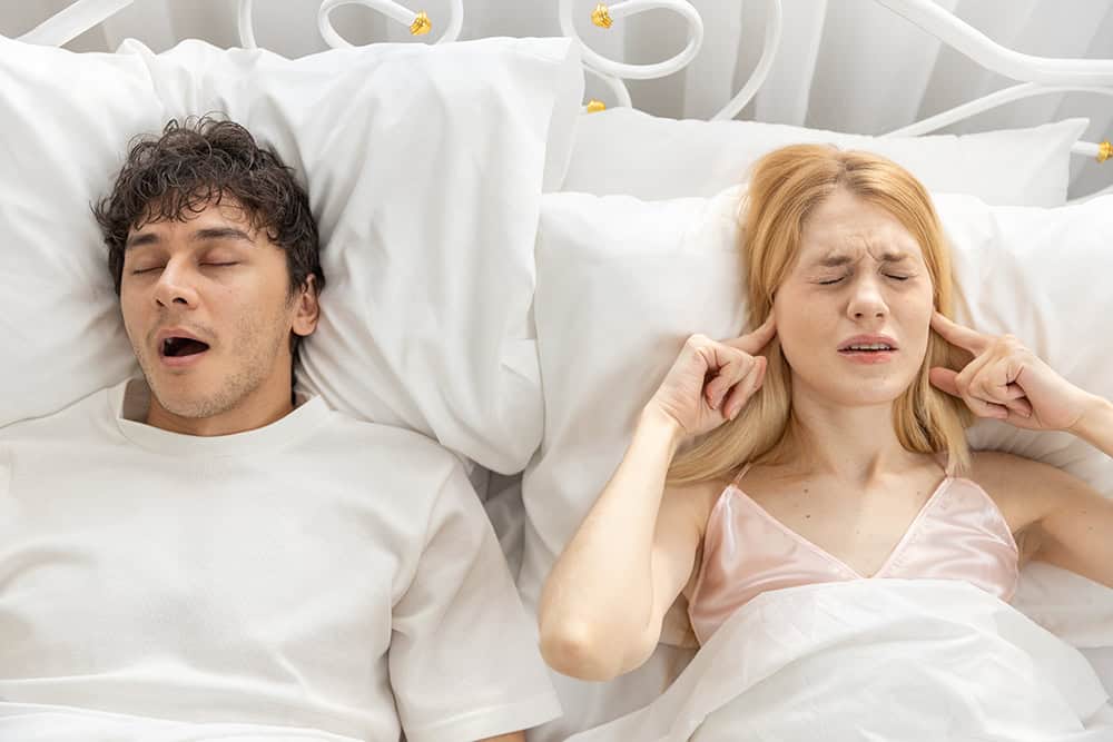 Online sleep apnea doctor - 2 treatments to transform life for man snoring in bed and stopping breathing in sleep while partner covers ears.
