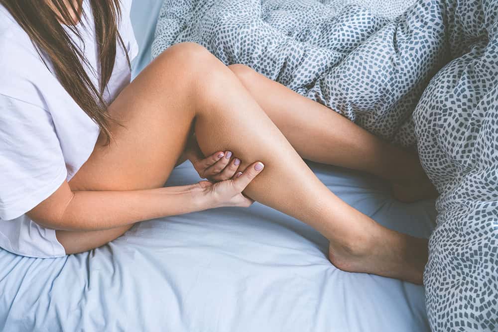 Restless Legs Syndrome Treatment — woman holding her leg in bed due to RLS discomfort.